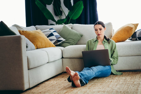 Charming woman relaxing on floor at home, using laptop, surrounded by comfortable modern decor, enjoying leisure timeの写真素材