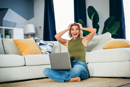 Young woman enjoying her leisure time at home with a laptop, expressing happiness and relaxation in...