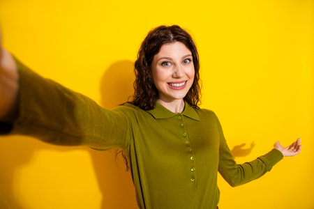 Cheerful young woman in green top extends her arms joyfully, posing with a radiant smile against a...