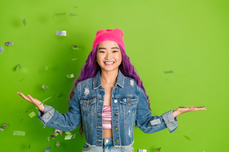 Cheerful young woman with dyed purple hair and casual style celebrating joyfully on vibrant green backgroundの写真素材
