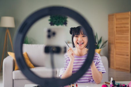Photo of pretty cheerful lady wear striped violet t-shirt apply mascara recording video modern device indoors room home houseの写真素材