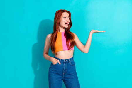Photo of pretty young girl hold empty space wear top isolated on vibrant teal color background