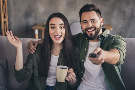 Photo of excited cheerful married guy lady wear casual shirts watching filn enjoy hot beverage indoors room home houseの写真素材