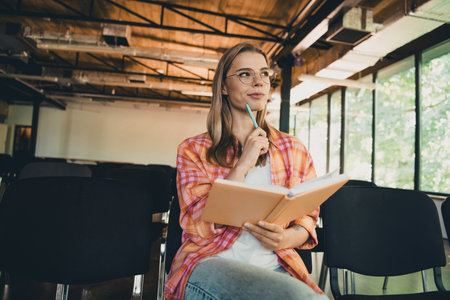 Photo of pretty young blonde girl minded write notebook wear plaid shirt coworking college auditorium listen speaker light interior indoorの写真素材