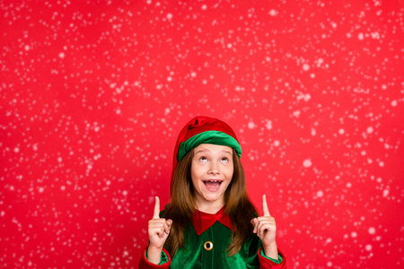 Portrait of impressed elf child in hat cap screaming wow omg showing adverts with her index finger...