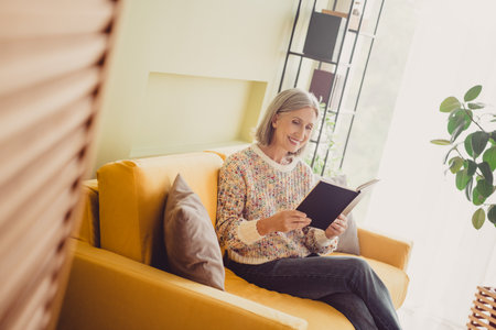Charming elderly woman enjoying leisure at home with a good book on a sunny weekend dayの写真素材
