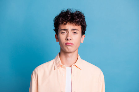 Portrait of a young man with curly brown hair wearing casual style against a blue background