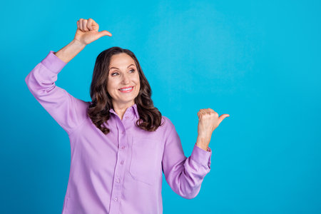 Photo of cheerful pretty lady dressed puple blouse showing two thumbs empty space isolated blue color backgroundの写真素材