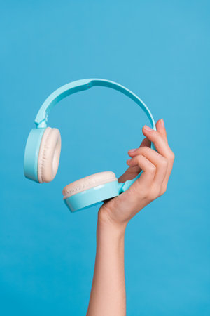 Cropped close up vertical photo of lady hand hold demonstrate wireless headphones isolated on blue color backgroundの写真素材