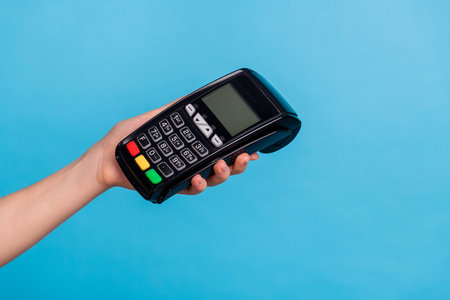 Cropped close up portrait of female hand hold payment terminal isolated on blue color backgroundの写真素材