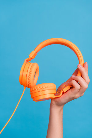Cropped close up vertical portrait of woman arm hold showing headphones isolated on blue color backgroundの写真素材