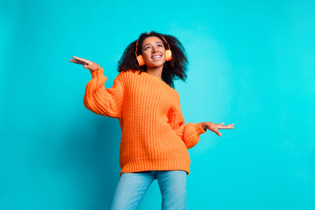 Photo portrait of attractive young woman dance have fun earphones dressed stylish knitted orange clothes isolated on cyan color backgroundの写真素材