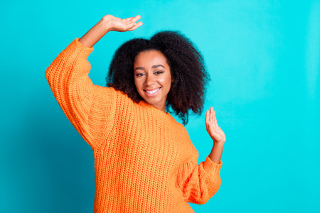 Photo portrait of attractive young woman dancing have fun dressed stylish knitted orange clothes isolated on cyan color backgroundの写真素材