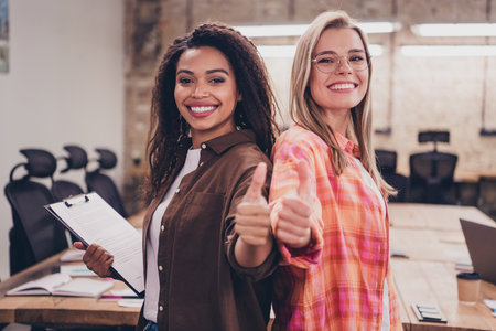 Photo of two corporate workers girls cooperate demonstrate thumb up business center office indoorsの写真素材