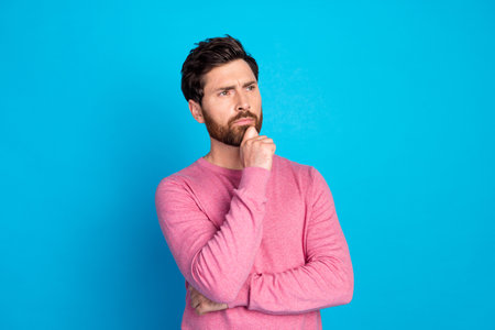 Thoughtful young man looking pensive in casual outfit against vibrant blue backgroundの写真素材