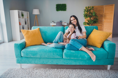 Photo of happy family cute mom and daughter enjoy weekend time together watch movie indoors living roomの写真素材