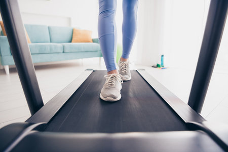 Woman jogging on treadmill in modern home interior with stylish activewear and natural daylight for a healthy lifestyleの写真素材