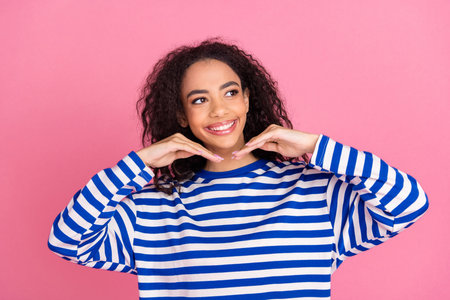 Portrait of nice young girl hands under chin look empty space wear striped pullover isolated on pink color backgroundの写真素材