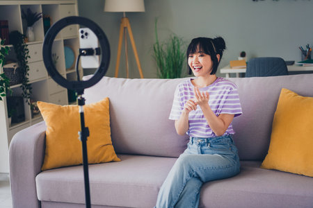 Photo of positive good mood woman dressed striped purple t-shirt vlogging modern gadget indoors house apartment roomの写真素材