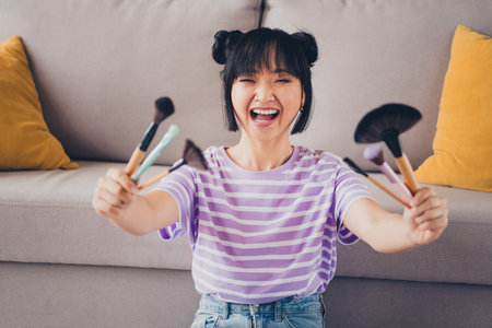 Photo of shiny cute girl dressed purple striped t-shirt showing visagiste tools indoors house apartment roomの写真素材