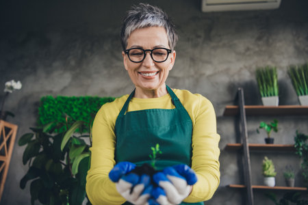 Photo of pensioner lady florist hands hold soil sprout wear green apron working flower shop studio small businessの写真素材