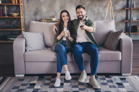 Photo of sweet happy married lady guy wear khaki shirts watching tv drinking coffee indoors room home houseの写真素材