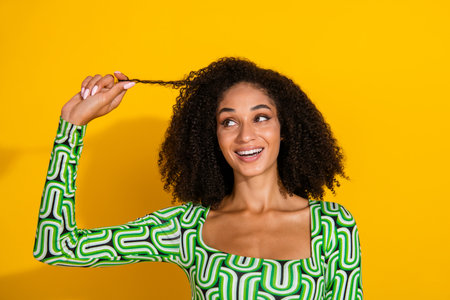 Charming young woman with curly hair in a vibrant green top against a yellow background, expressing joy and happiness.の写真素材