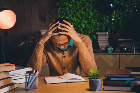 Young student studying intensely in dimly lit home office at night with focused expression...
