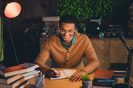 Young student in casual attire studying at home surrounded by books and natural light, focusing on college assignments indoorsの写真素材