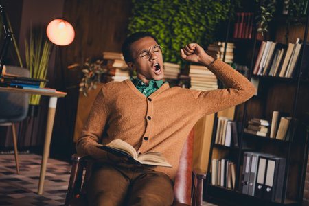 Young student yawning while reading a book in his stylish home studyの写真素材