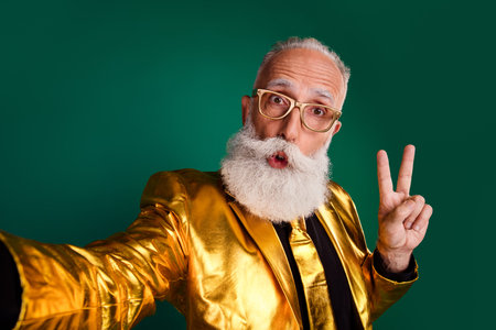 Charismatic elderly gentleman in a glowing golden suit poses playfully against a vibrant green background.の写真素材