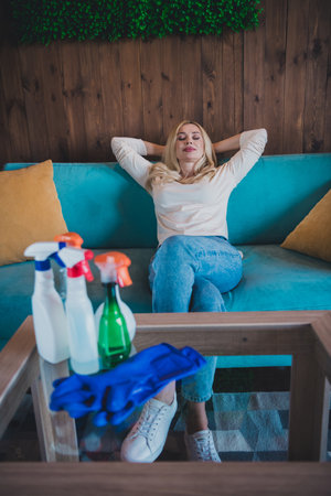 Vertical photo of positive good mood woman dressed white shirt relaxing arms behind head doing housework indoors house apartment roomの写真素材