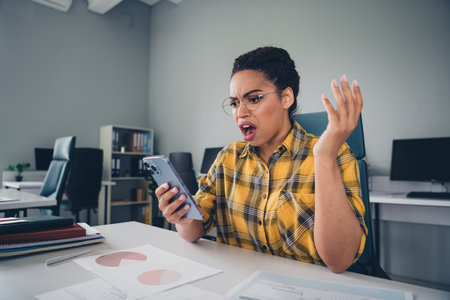 Photo of lovely young lady irritated angry hold device read news dressed yellow plaid shirt comfortable startup office loft room interiorの写真素材