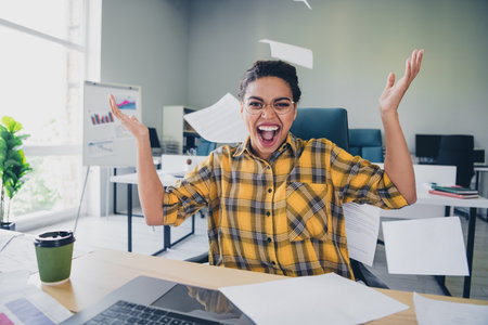 Photo of young woman excited throw papers scream wear yellow plaid shirt comfortable modern office loft room interior indoors workspaceの写真素材