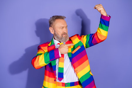 Elderly man in rainbow suit posing against purple background showcasing pride and eccentric style