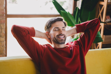 Young man enjoying a peaceful moment at home in a cozy sweater, embracing relaxation in a comfortable living spaceの写真素材