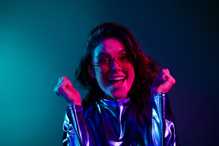 Portrait of stunning young woman raise fists wear shiny dress neon light dark blue backgroundの写真素材