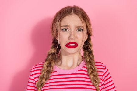 Confused young woman with braids and bold red lips standing against a pink background in a stylish summer outfitの写真素材