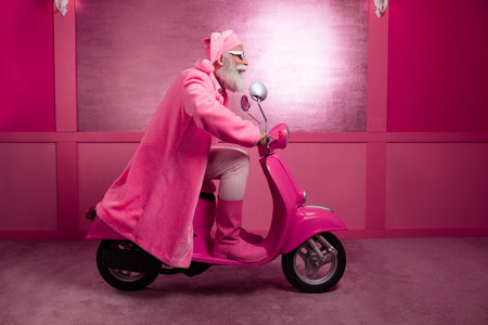 Full size portrait of excited aged man wear pink santa outfit hat coat boots drive bike studio corridor backgroundの写真素材