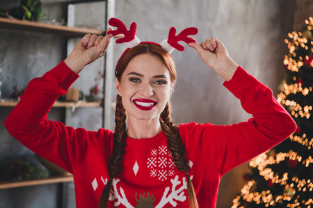 Portrait of nice young woman hands touch reindeer horns headband wear red new year xmas sweater flat indoorsの写真素材
