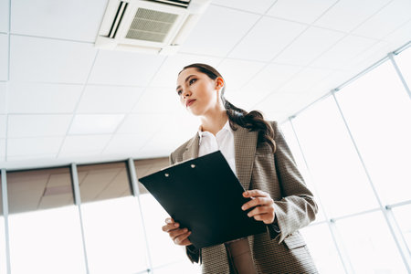 Young specialist businesswoman holding a clipboard in a professional office environment under bright...