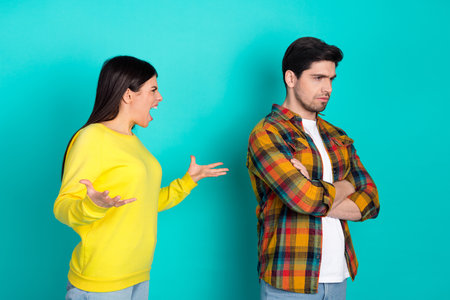 Young couple in a heated disagreement with expressive gestures against a vibrant turquoise background, showcasing emotionsの写真素材