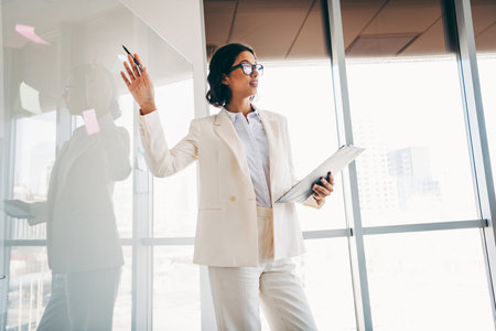 Professional businesswoman in a bright office presenting ideas with confidence and elegance for a corporate presentationの写真素材