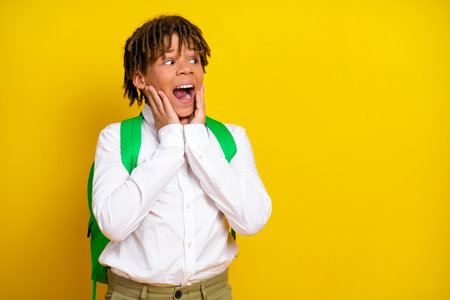Excited schoolboy expressing surprise and joy while wearing a backpack on a vibrant yellow backgroundの写真素材