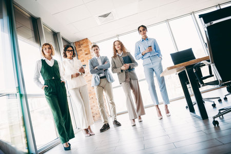 Group of professionals in stylish attire standing confidently at a modern workplace, representing teamwork and office collaborationの写真素材