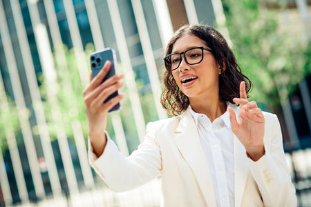 Successful young businesswoman taking a selfie while discussing work outdoors in a modern urban setting wearing formal attireの写真素材