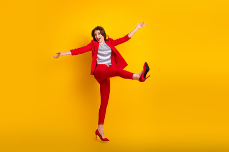 Young woman in red suit posing joyfully with cheerful gestures against a vibrant yellow background illustrating happinessの写真素材