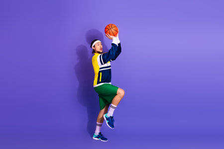 Energetic young man posing with basketball in retro sportswear on vibrant violet background...