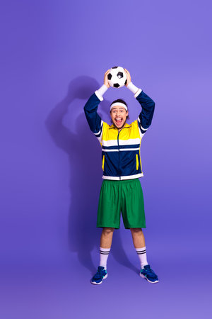 Young energetic athlete holding soccer ball against a vibrant purple background celebrating fitness and sportsmanshipの写真素材