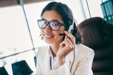 Confident businesswoman in an office environment wearing a headset, engaged in communication,...